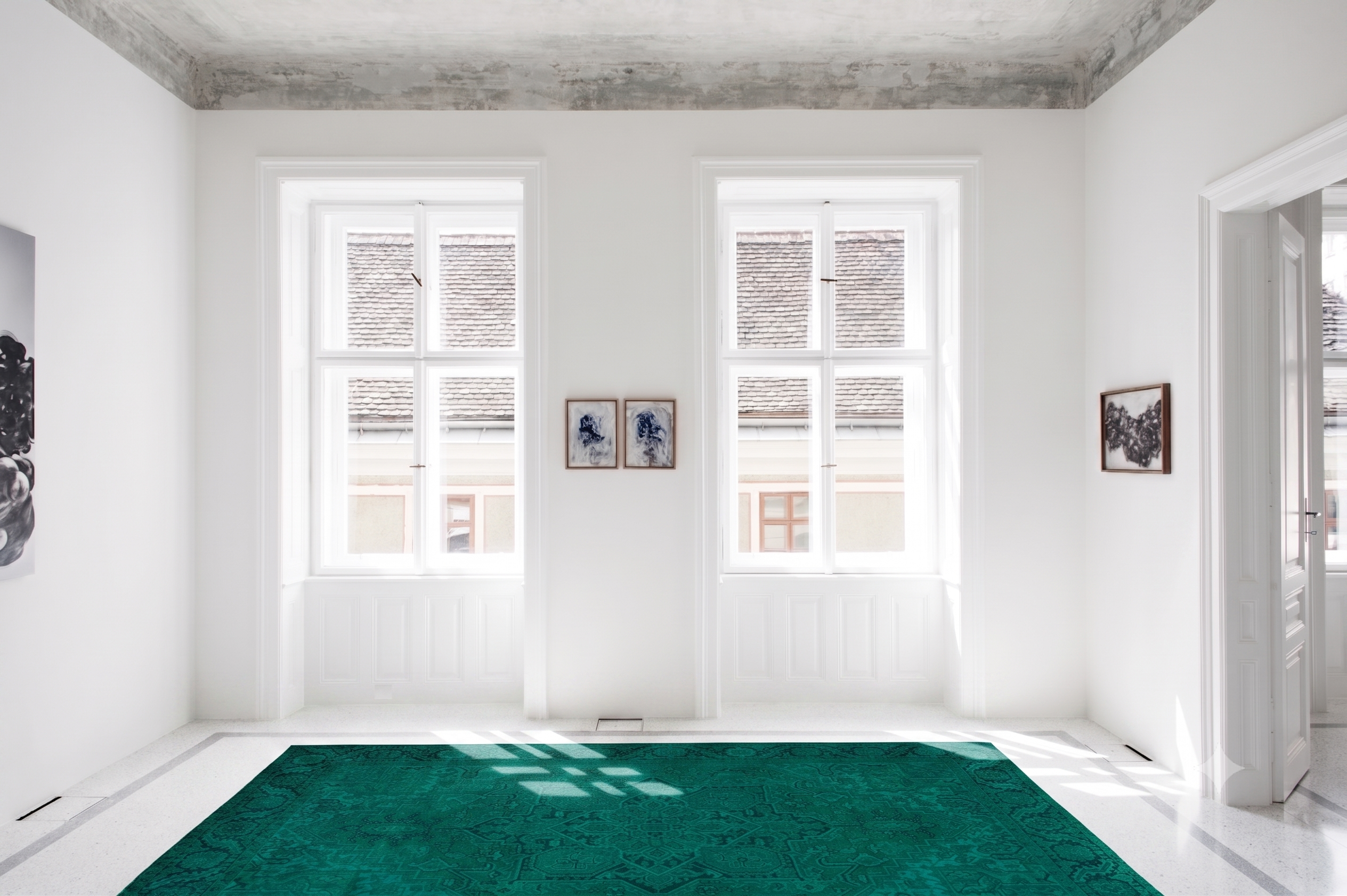 Heller Galerieraum mit weißem Terrazzoboden, zwei hohen Fenstern und einem großen petrolfarbenen Orientteppich mit klassischem Muster